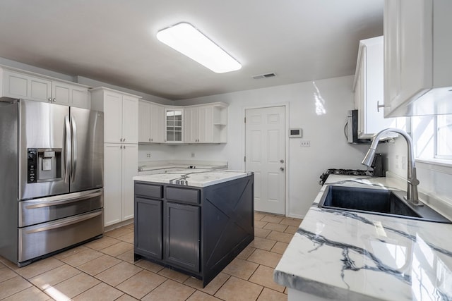 kitchen with visible vents, a sink, a center island, stainless steel fridge, and white cabinets