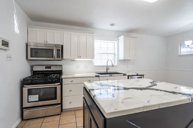 kitchen with a sink, a center island, white cabinetry, appliances with stainless steel finishes, and light tile patterned floors