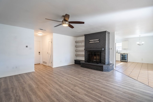 unfurnished living room featuring a brick fireplace, wine cooler, light wood-style floors, and visible vents