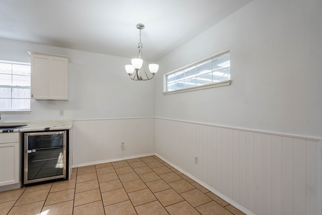 unfurnished dining area with a sink, wine cooler, a notable chandelier, and wainscoting