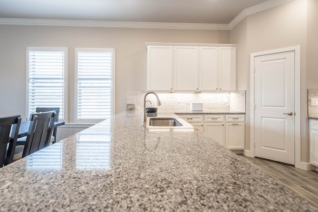 kitchen featuring crown molding, light stone countertops, tasteful backsplash, white cabinetry, and sink