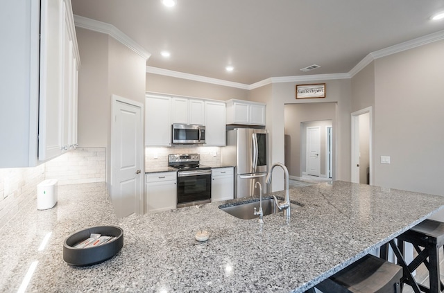 kitchen with appliances with stainless steel finishes, white cabinetry, decorative backsplash, sink, and a breakfast bar area