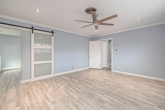 empty room with ceiling fan, ornamental molding, a barn door, and light hardwood / wood-style floors