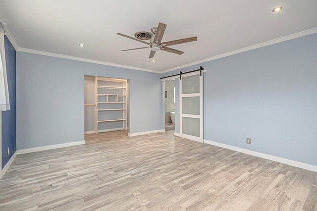 unfurnished bedroom featuring ornamental molding, a barn door, a closet, and light wood-type flooring