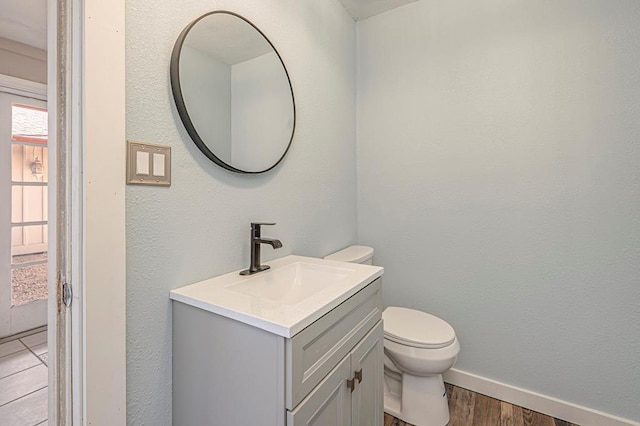 bathroom with toilet, wood finished floors, vanity, and baseboards