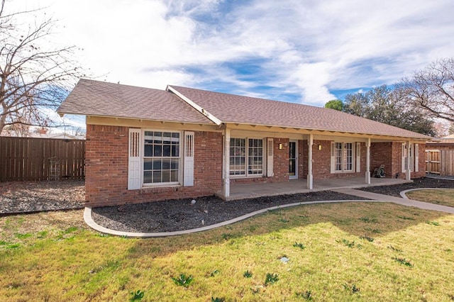 back of property with brick siding, a shingled roof, fence, a lawn, and a patio area