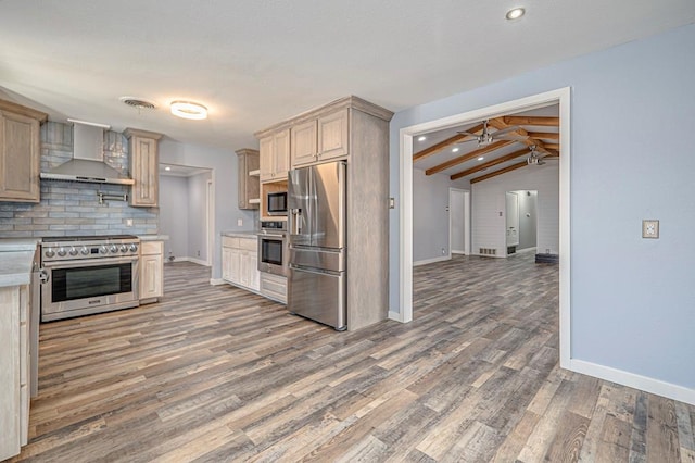 kitchen featuring wall chimney range hood, dark wood-type flooring, appliances with stainless steel finishes, vaulted ceiling with beams, and decorative backsplash