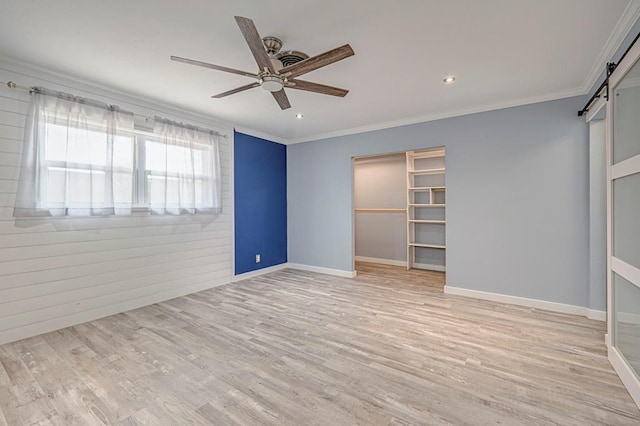 unfurnished bedroom featuring a barn door, baseboards, ceiling fan, light wood-style flooring, and crown molding