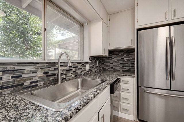 kitchen with backsplash, appliances with stainless steel finishes, a sink, white cabinets, and stone countertops
