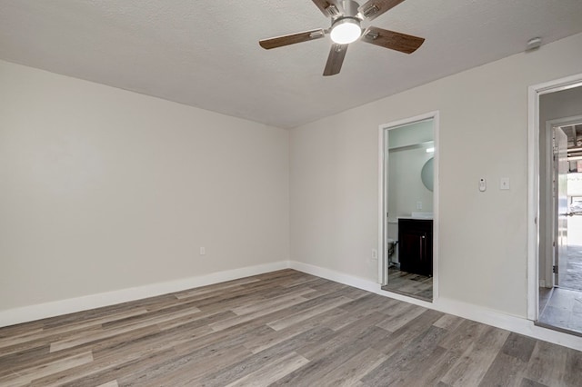 unfurnished bedroom with baseboards, a ceiling fan, wood finished floors, and connected bathroom