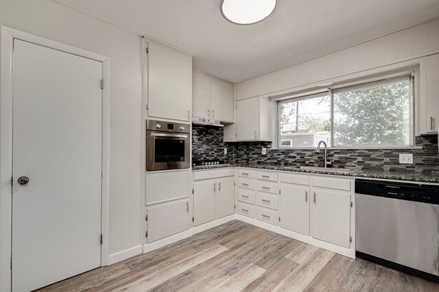 kitchen featuring backsplash, appliances with stainless steel finishes, light wood-type flooring, a sink, and white cabinetry