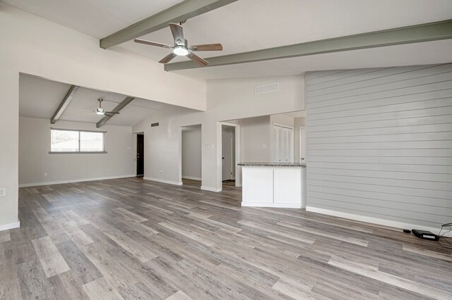 unfurnished living room with a ceiling fan, visible vents, wood finished floors, baseboards, and vaulted ceiling with beams