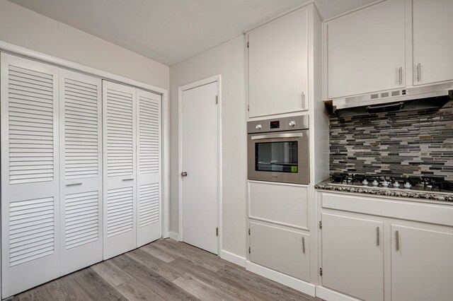 kitchen featuring white cabinets, light wood-style flooring, stainless steel appliances, decorative backsplash, and under cabinet range hood