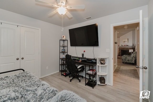 bedroom featuring visible vents, a fireplace with raised hearth, a ceiling fan, light wood-style flooring, and a closet