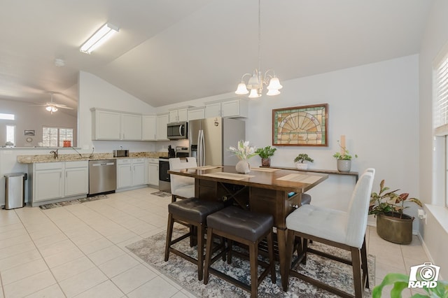 dining space featuring ceiling fan with notable chandelier, vaulted ceiling, and light tile patterned floors