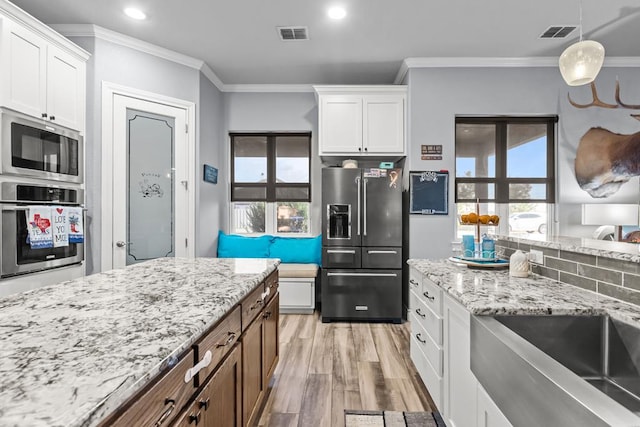 6811 Elkins Rd, Midland, TX 79705 - kitchen with appliances with stainless steel finishes, white cabinets, ornamental molding, light wood-style flooring, and light stone countertops