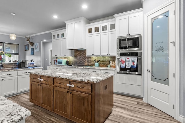 6811 Elkins Rd, Midland, TX 79705 - kitchen with stainless steel appliances, decorative backsplash, light wood-style flooring, white cabinetry, and a center island