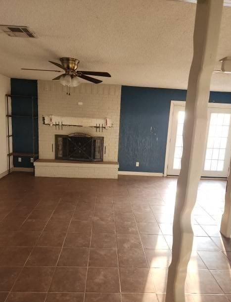 unfurnished living room featuring a fireplace, a textured ceiling, dark tile patterned floors, and ceiling fan