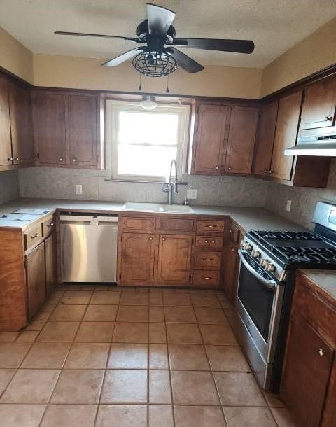 kitchen with appliances with stainless steel finishes, backsplash, extractor fan, sink, and light tile patterned floors