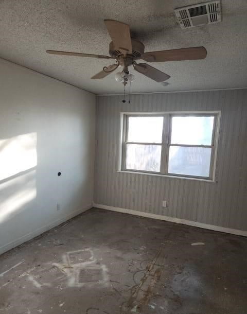 unfurnished room with plenty of natural light, ceiling fan, a textured ceiling, and wooden walls