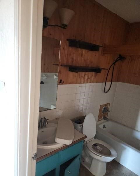 full bathroom featuring vanity, wood walls, toilet, tile walls, and tub / shower combination