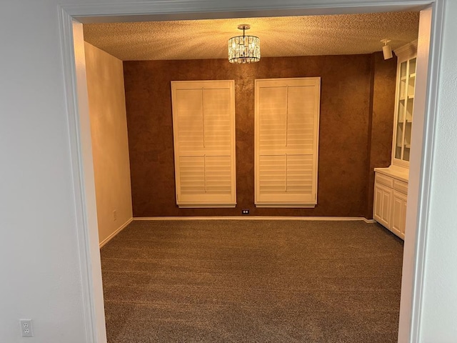 unfurnished room with an inviting chandelier, baseboards, dark carpet, and a textured ceiling