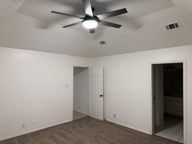 unfurnished bedroom with visible vents, ensuite bathroom, a textured ceiling, and carpet flooring