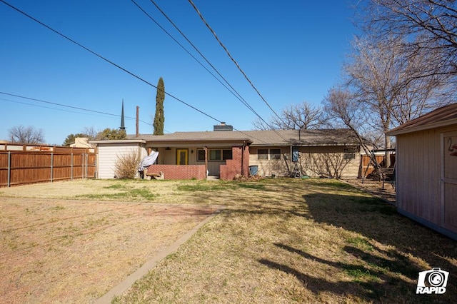 back of property featuring brick siding, a chimney, an outdoor structure, and fence