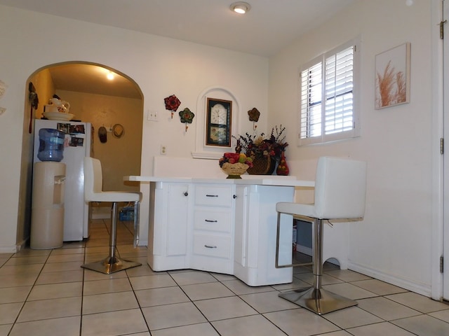 kitchen featuring light tile patterned floors, light countertops, arched walkways, and white cabinets