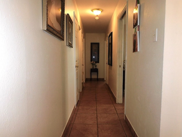 hall featuring dark tile patterned floors and baseboards