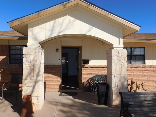 view of exterior entry with roof with shingles and brick siding