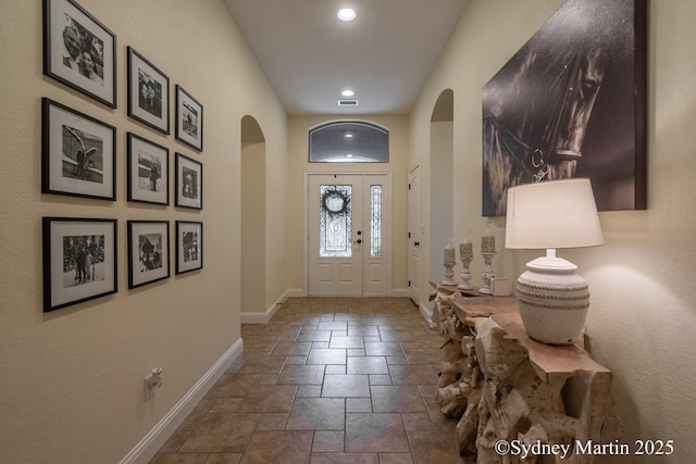 foyer featuring arched walkways, stone tile floors, baseboards, and recessed lighting