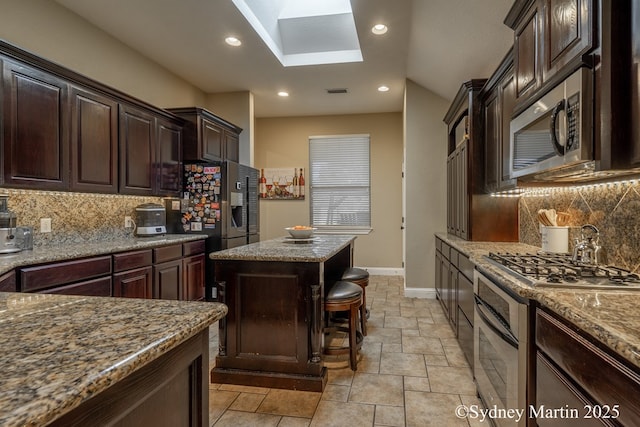 kitchen featuring stainless steel appliances, a skylight, baseboards, a center island, and backsplash
