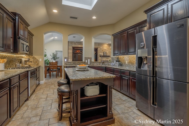 kitchen featuring stainless steel appliances, open shelves, stone tile flooring, tasteful backsplash, and a center island