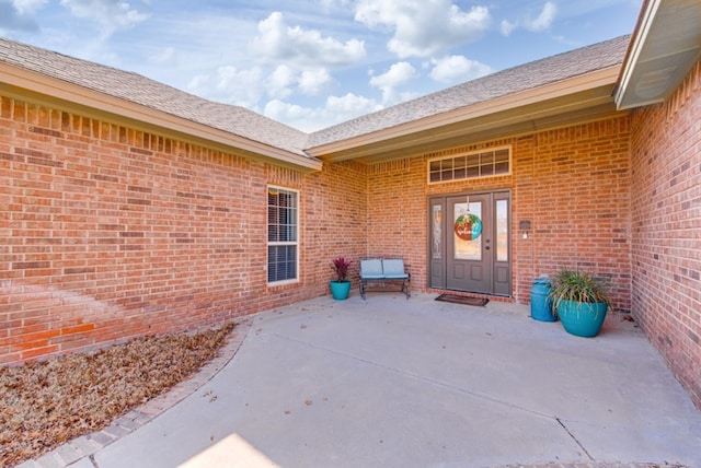 entrance to property featuring brick siding and roof with shingles