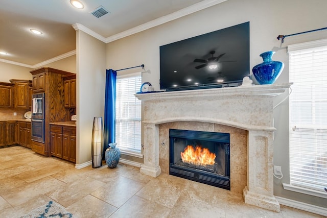 living area featuring ceiling fan, a premium fireplace, visible vents, baseboards, and ornamental molding