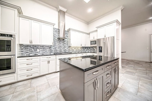 kitchen featuring dark stone counters, wall chimney exhaust hood, ornamental molding, appliances with stainless steel finishes, and a kitchen island