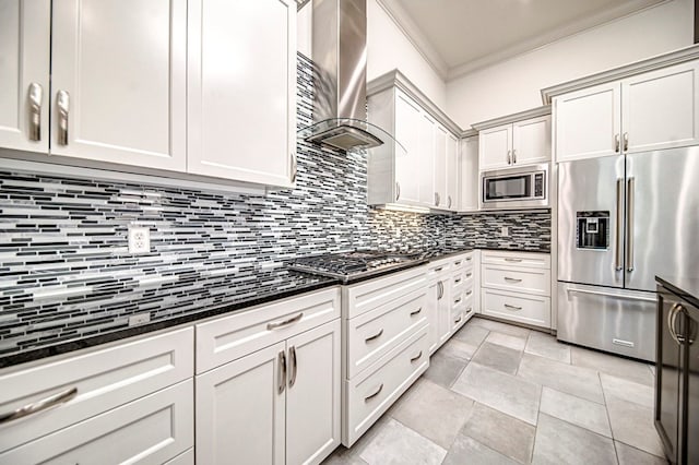 kitchen featuring wall chimney exhaust hood, dark stone countertops, crown molding, decorative backsplash, and appliances with stainless steel finishes