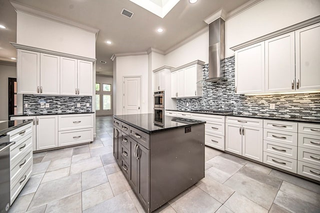 kitchen featuring tasteful backsplash, crown molding, white cabinets, and wall chimney range hood