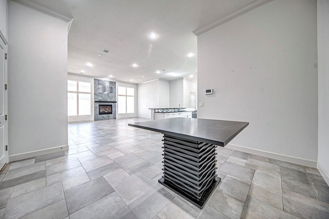 kitchen with a center island, crown molding, a kitchen bar, white cabinetry, and a tiled fireplace