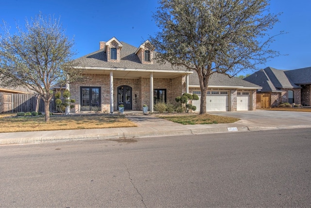 view of front facade with french doors, brick siding, an attached garage, fence, and driveway