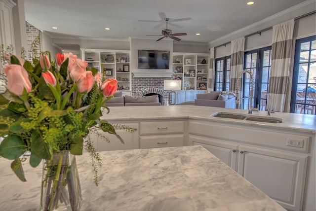 kitchen featuring a fireplace, ornamental molding, open floor plan, white cabinetry, and a sink