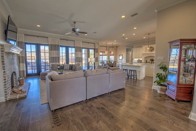 living area with dark wood-type flooring, a brick fireplace, visible vents, and crown molding