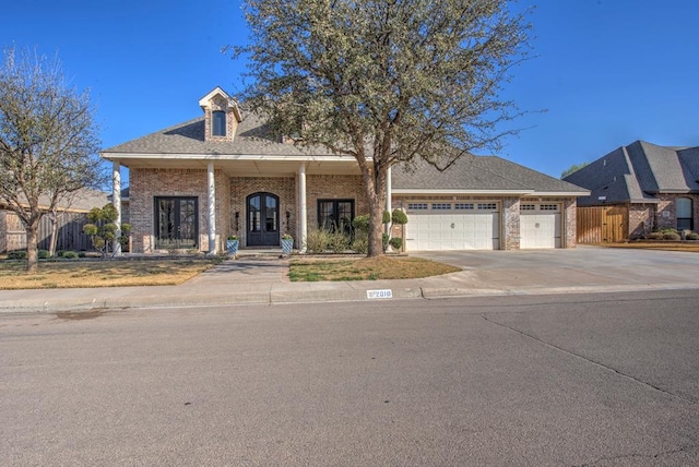 view of front of house featuring an attached garage, brick siding, fence, driveway, and french doors