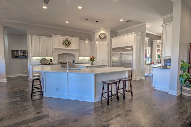 kitchen featuring a breakfast bar, dark wood-style flooring, a sink, an island with sink, and stainless steel built in refrigerator