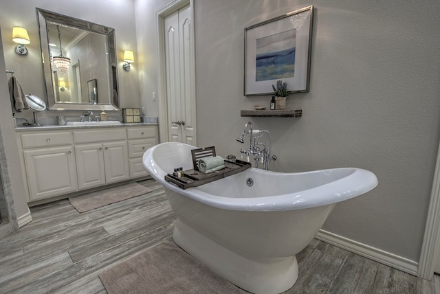 bathroom featuring a textured wall, wood finished floors, vanity, baseboards, and a freestanding bath