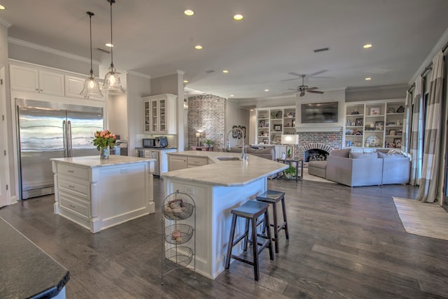 kitchen with stainless steel built in fridge, a center island with sink, ornamental molding, and a sink