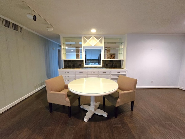 dining area featuring ornamental molding, rail lighting, a textured ceiling, and dark wood-type flooring