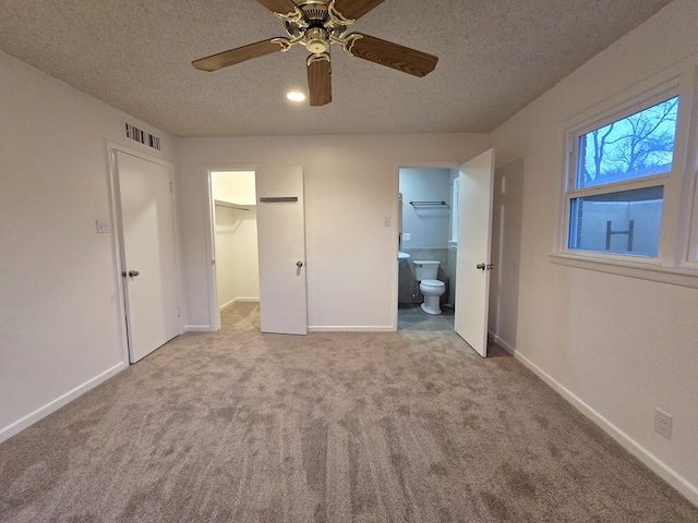 unfurnished bedroom with light carpet, ensuite bath, ceiling fan, a spacious closet, and a textured ceiling