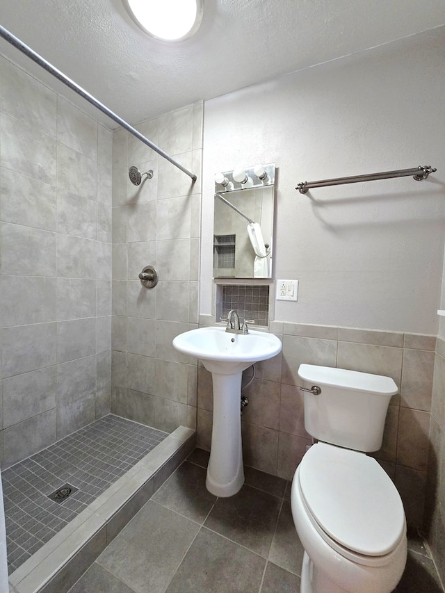 bathroom featuring a textured ceiling, tiled shower, tile walls, tile patterned flooring, and toilet